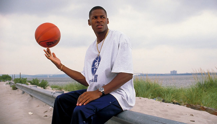 Ray Allen spins a basketball on his index finger while sitting on a guardrail at a beach.