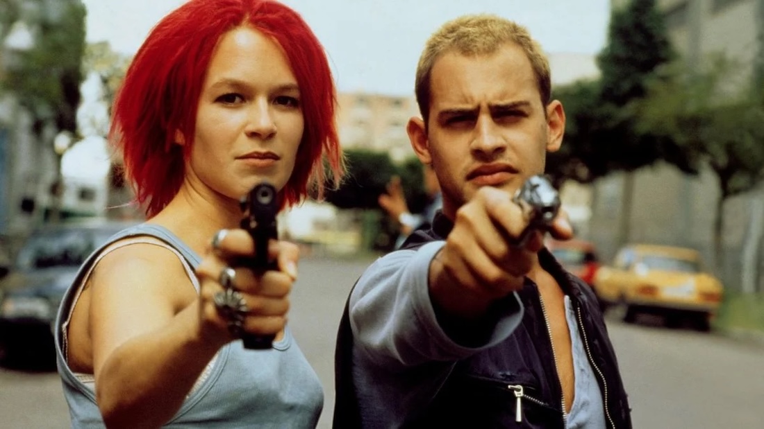 A man and a woman stare forward and each point a gun at the camera.
