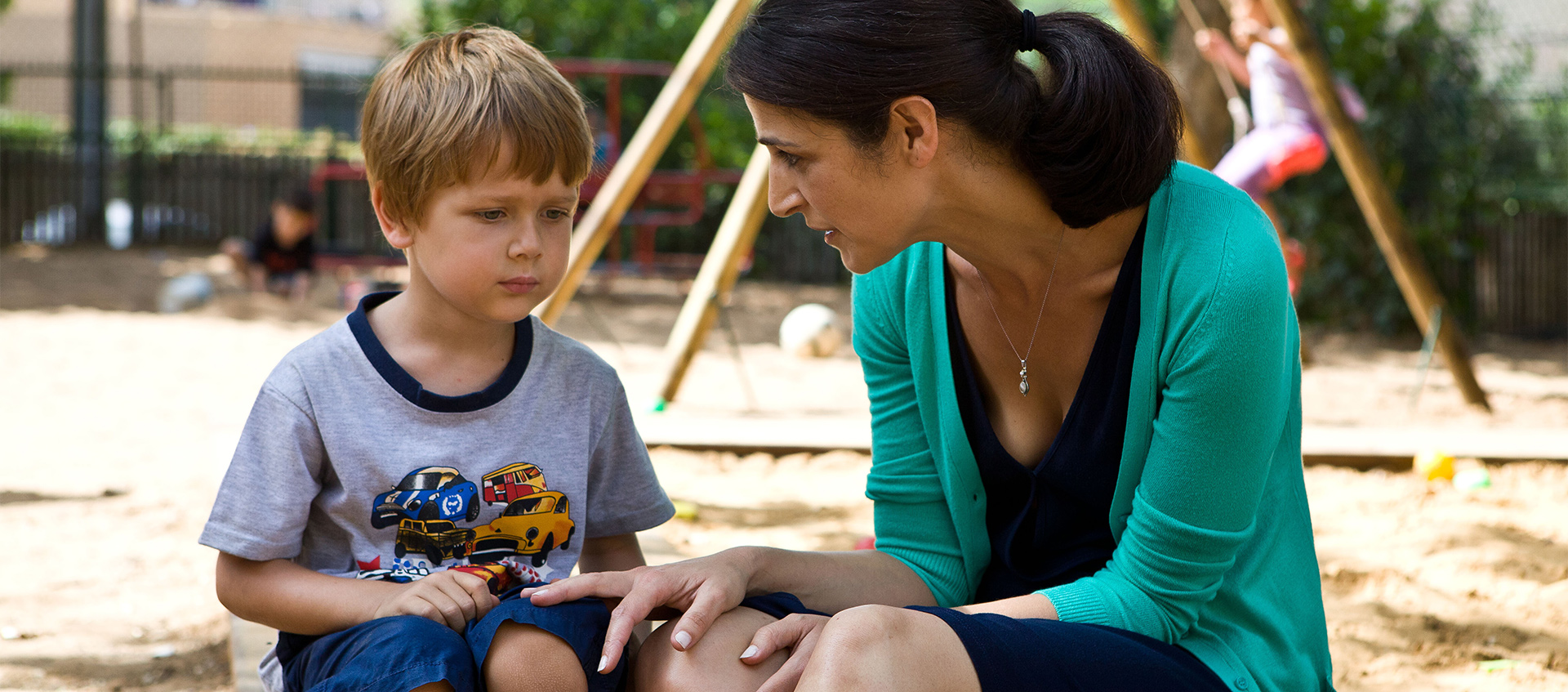 A young boy and a woman sitting and talking in a playground.