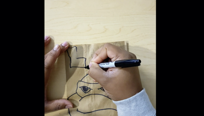 The hands of artist Alexander Chisley are seen drawing text with Sharpie marker above a drawing of a Teenage Mutant Ninja Turtle on a paper bag