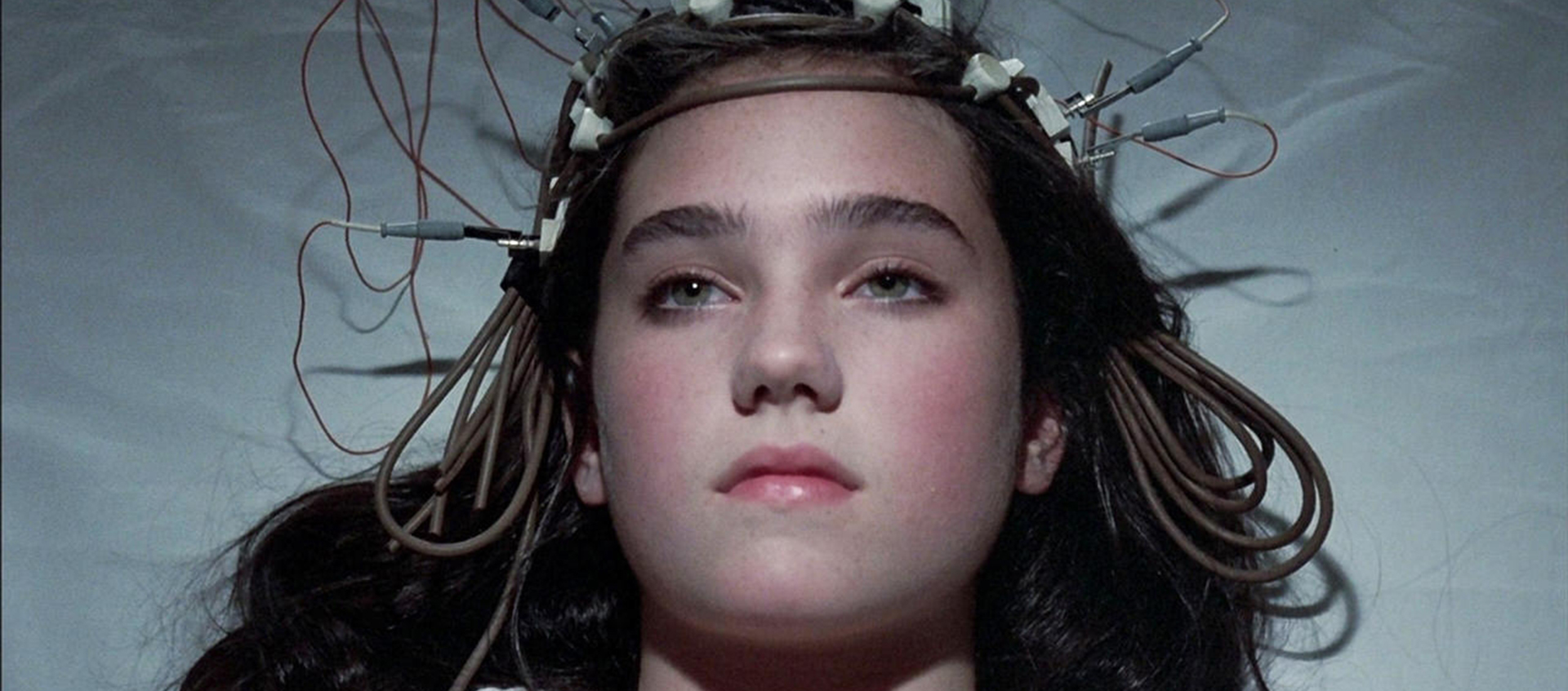 A young woman is lying on her back on a white sheet with wires attached to her head. She looks calm.