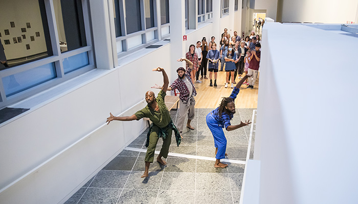 A group of people watch three Black men perform a dance in the Wex galleries.