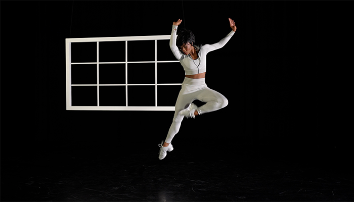 A woman jumping in the air on a black background with a white window behind her.