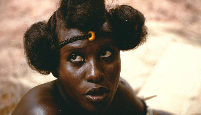 A Black woman (Sarraounia, the main character of the film) looks up towards the top left of the frame. 
