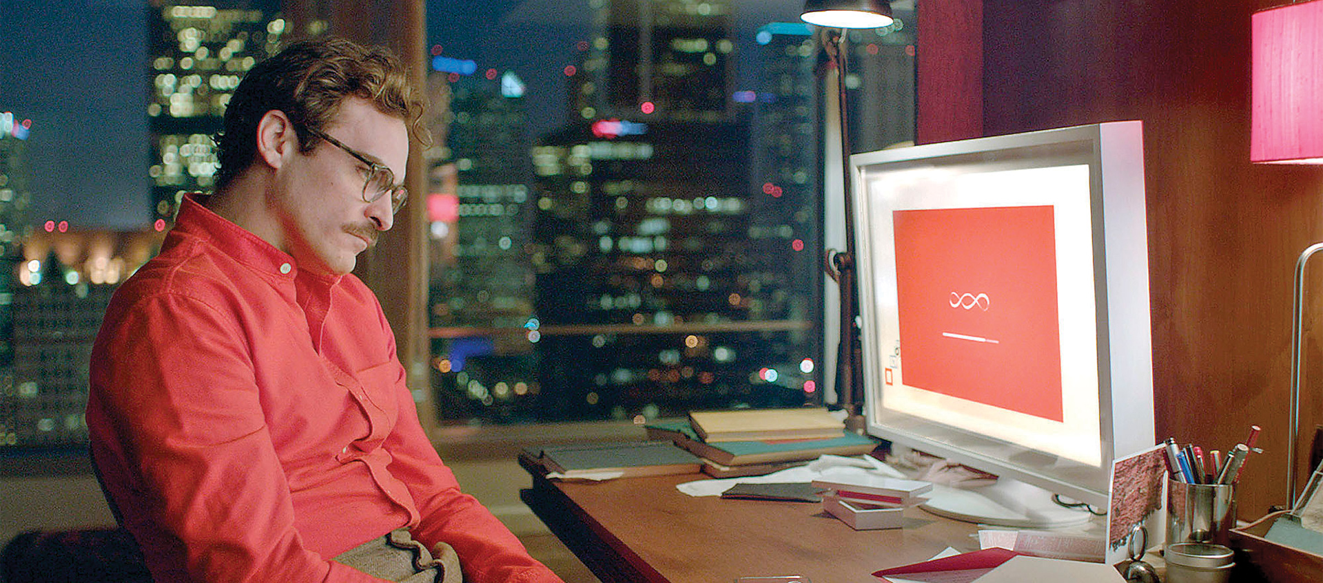 a man in a red shir looking at computer computer screen in an office