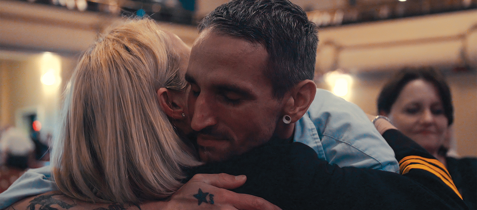 a man with arm tattoo hugging a blond woman