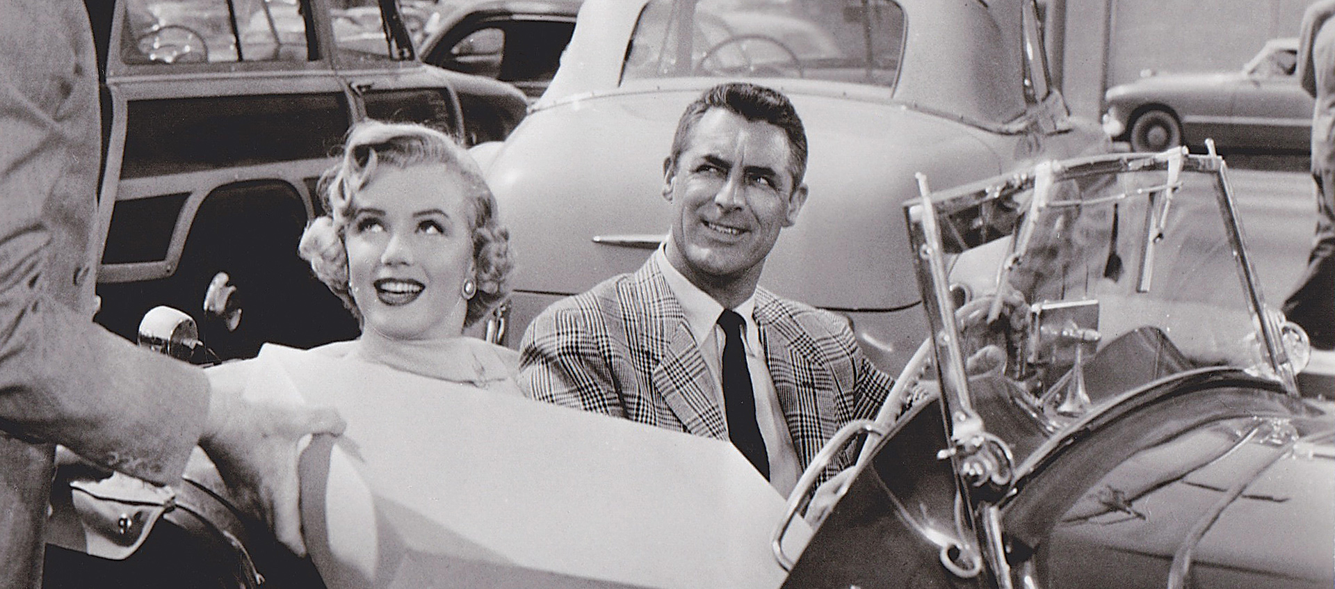 a man and woman in a two-doots, open roof car; the woman is handed a box