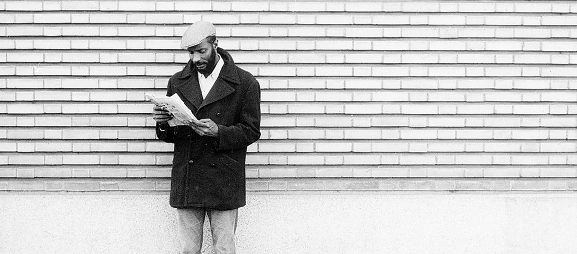 Man reading newspaper against wall; Soleil Ô