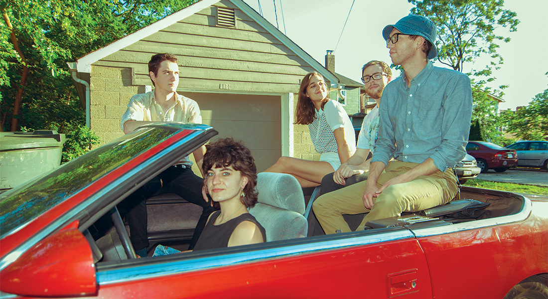 two women and three men sitting in a red convertible