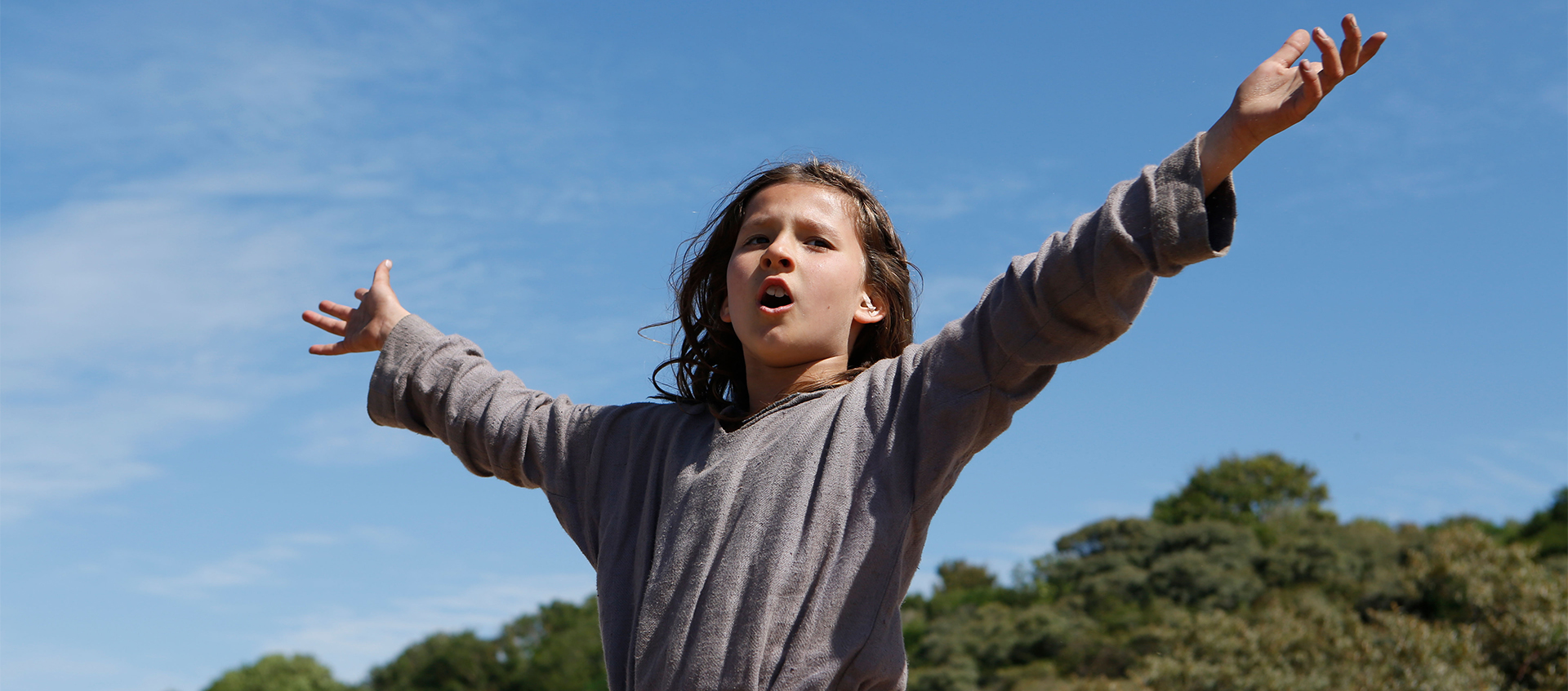 Promotional still image of a young woman singing with arms outstretched, from the 2018 Bruno Dumont film Jeannette: The Early Childhood of Joan of Arc