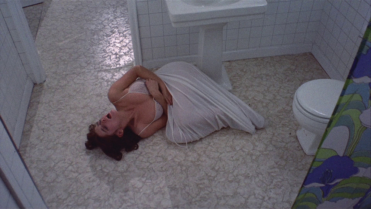 Film still of a woman writhing in pain on a bathroom floor