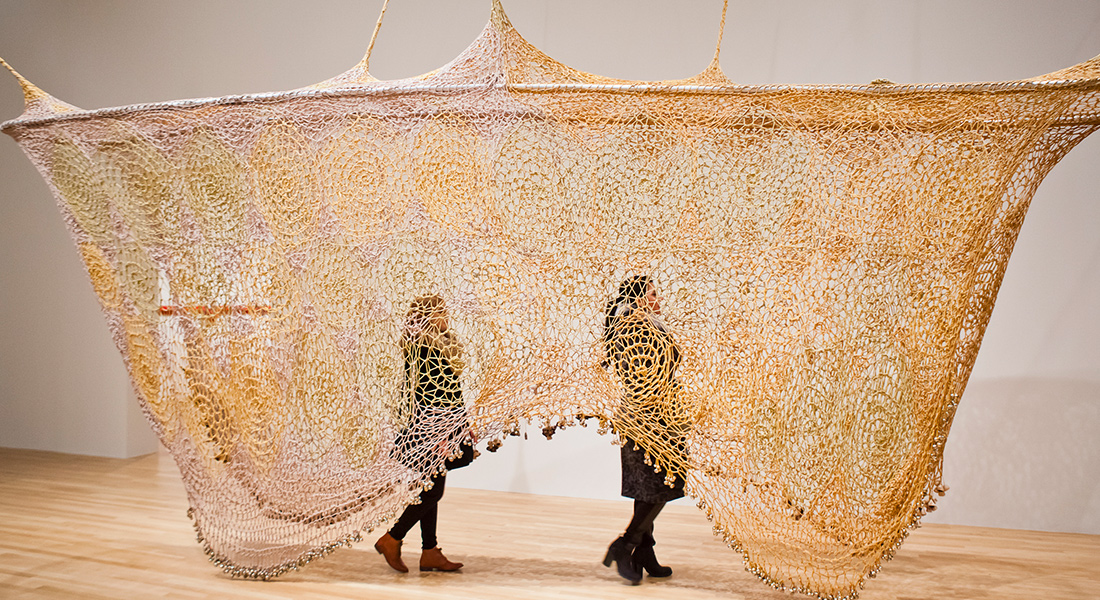 Patrons walk through a textile sculpture hanging from the ceiling in the Wexner Center galleries