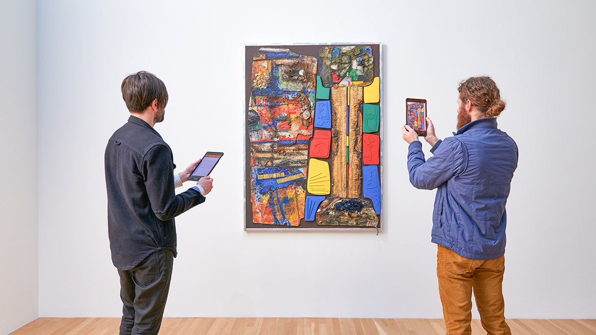 Patrons using an interactive app to view a mixed media work by Noah Purifoy