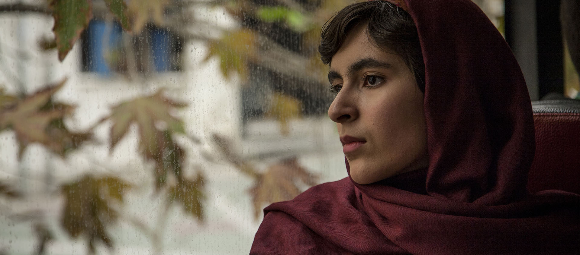 A young woman in a hijab steering out the window of a bus