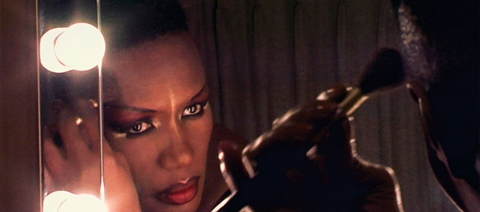 a film still of grace jones applying make up in front of a mirror