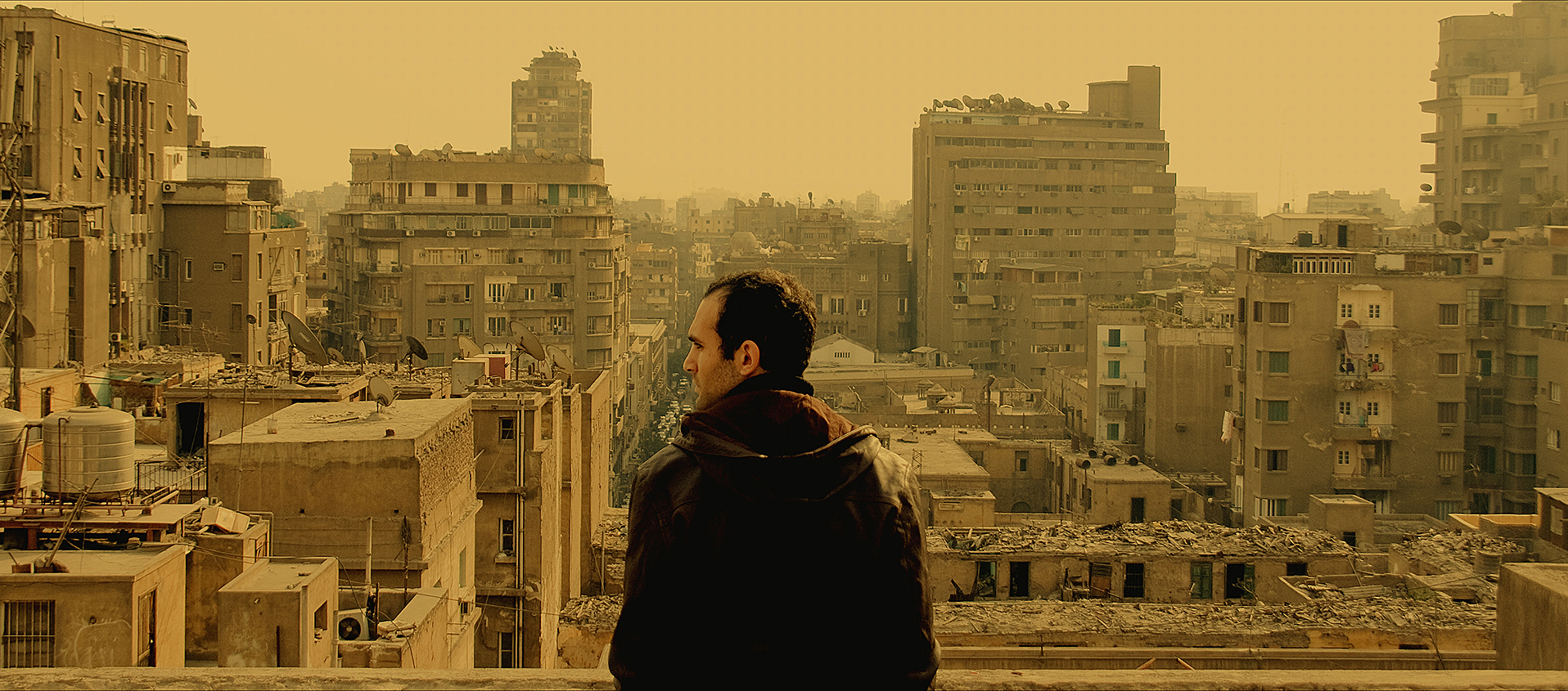 A man seen from behind, looking across a yellow-tinted cityscape