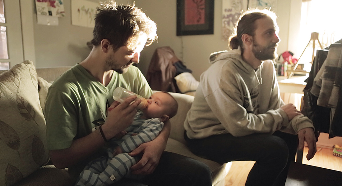 Two men on a couch, one holds a baby