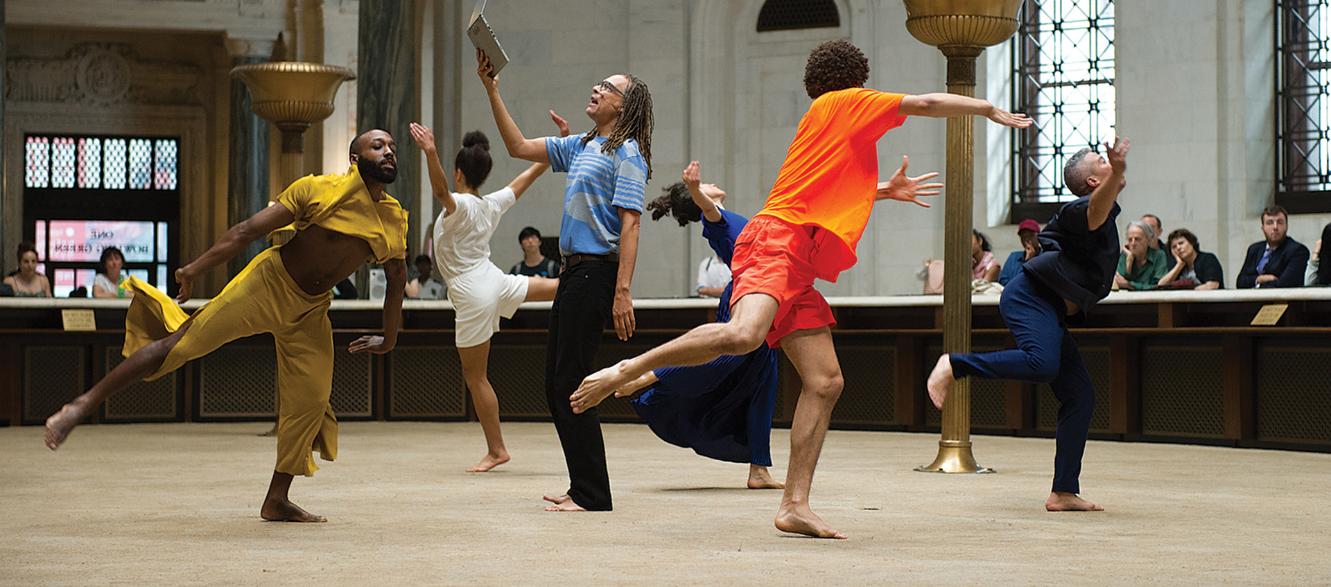 Five dancers encircle a sixth performer holding a laptop