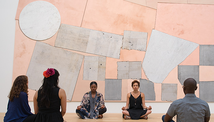 a group of people practicing yoga with an art work installation behind them