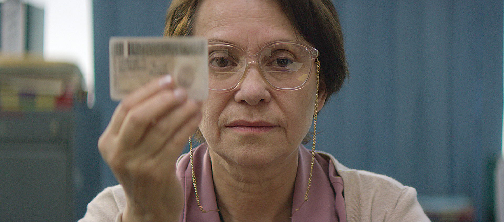 Older woman in glasses holding ID
