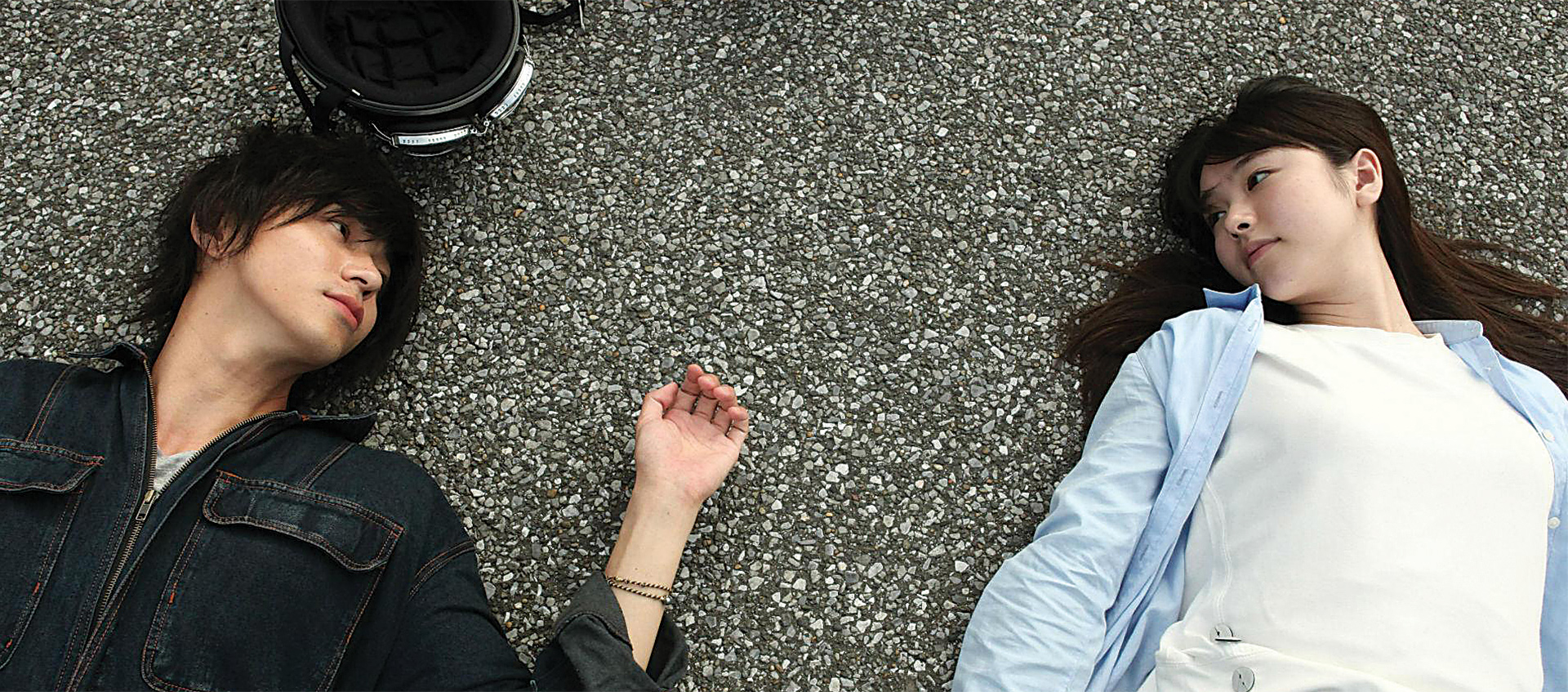 A boy and a girl lay on the asphalt staring at one another
