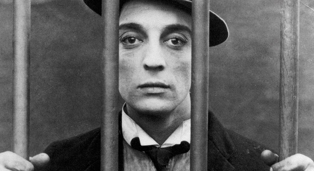 A man in a suit, tie and hat stands behind bars