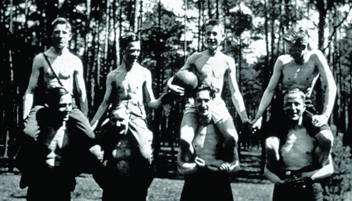 A group of men sitting on top of each others shoulders on an outdoor basketball court