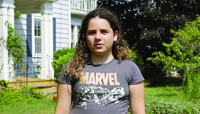 A girl in a Marvel T-shirt stands in front of a home