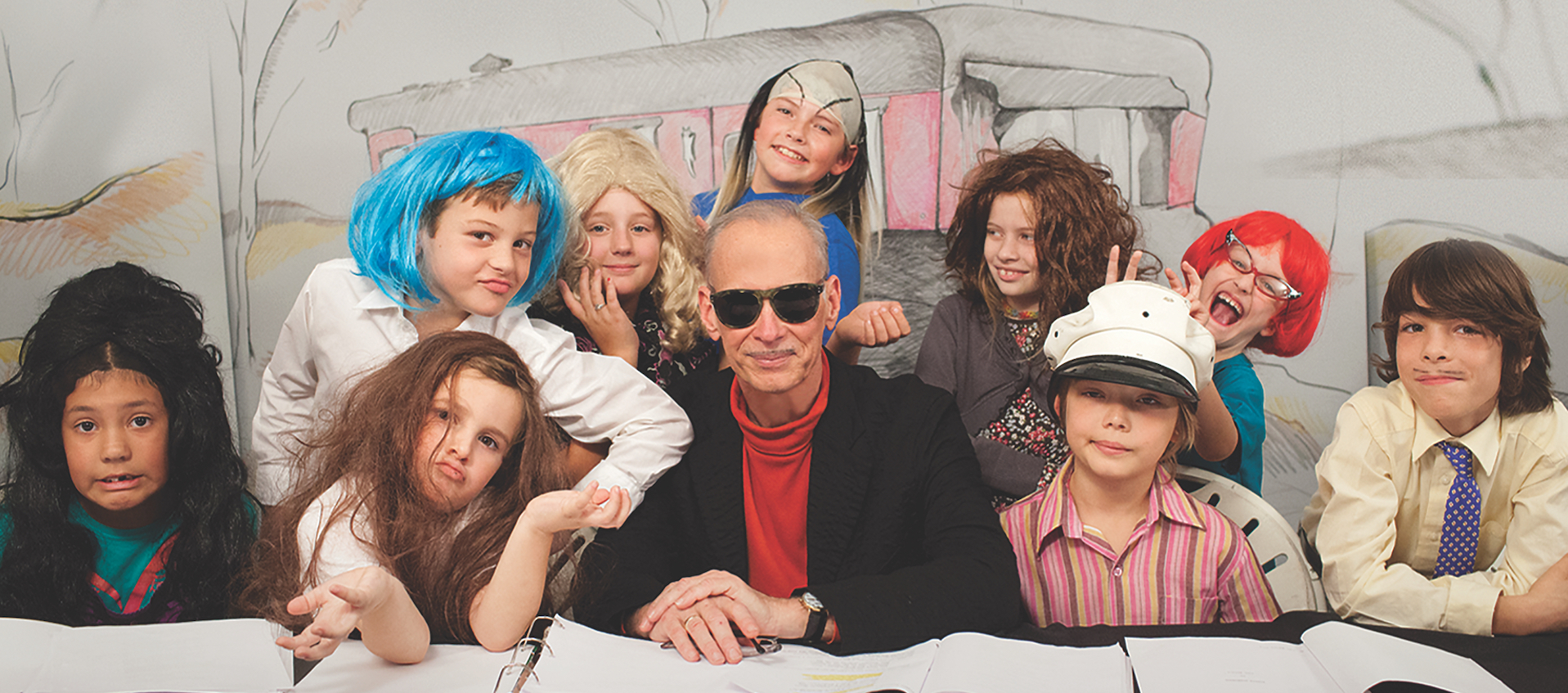 Artist and filmmaker John Waters sits surrounded by the all-children cast of Kiddie Flamingos, the G-rated retelling of Pink Flamingos