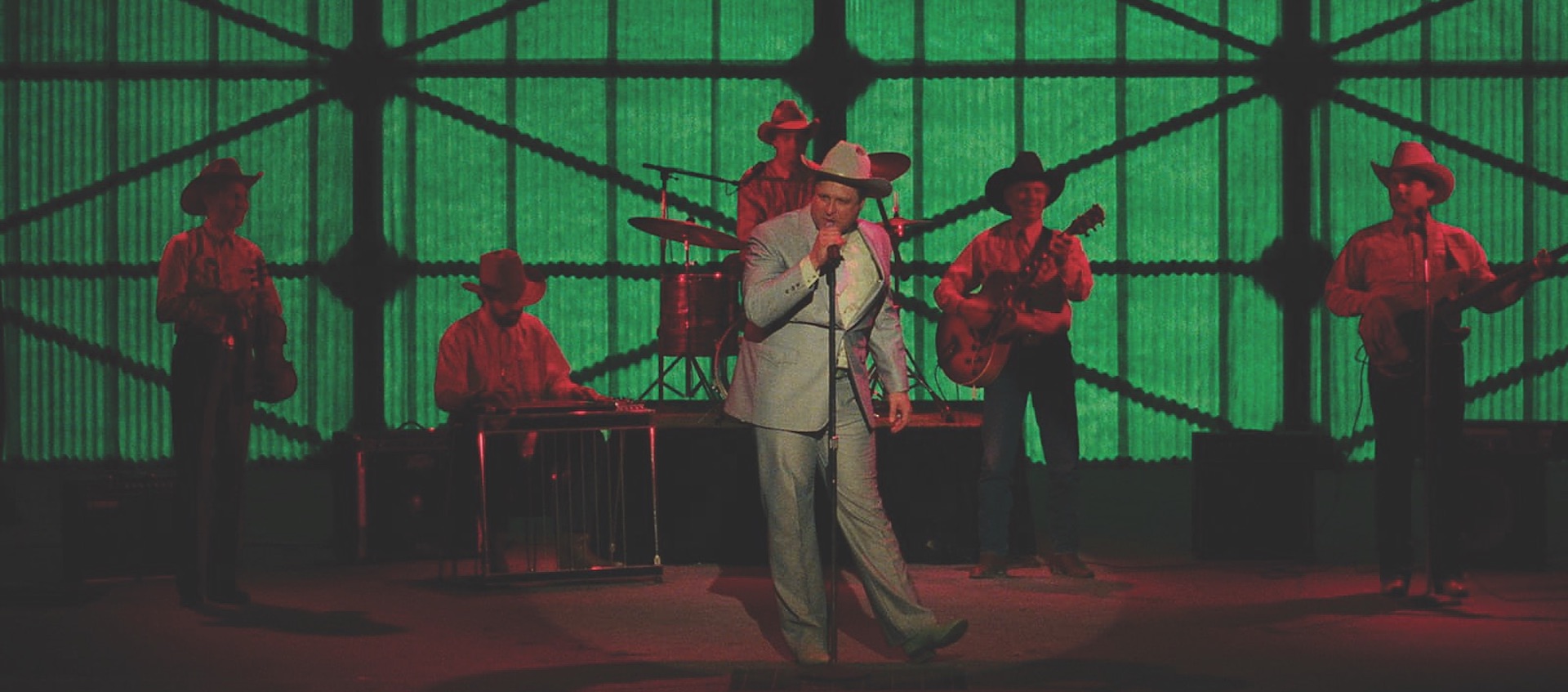 John Goodman sings on stage in a cowboy outfit in a scene from David Byrne's movie True Stories