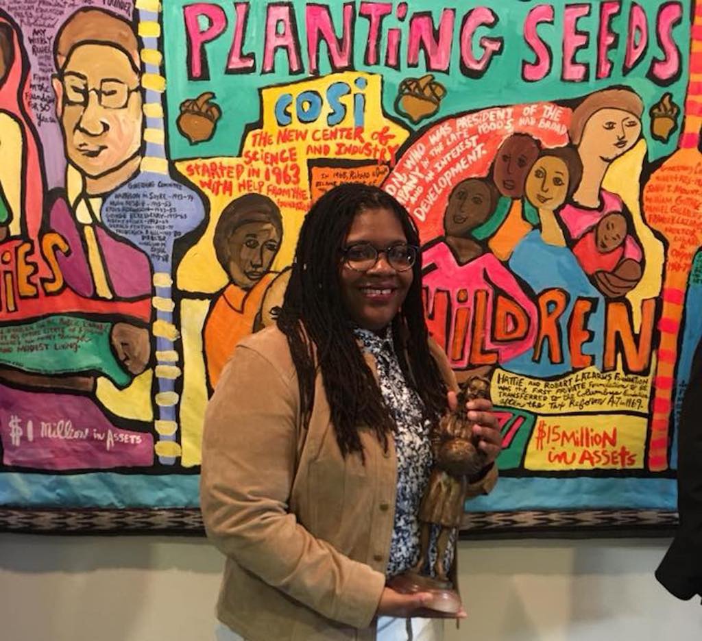 Photo of Columbus Black International Film Festival Director Cristyn Steward standing in front of the Aminah Robinson mural at the Columbus Metropolitan Library. Photo: Erica M. Allen