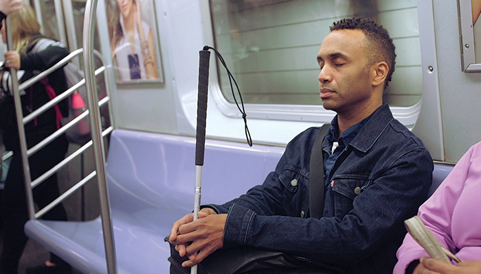 Man holding cane, sitting on train
