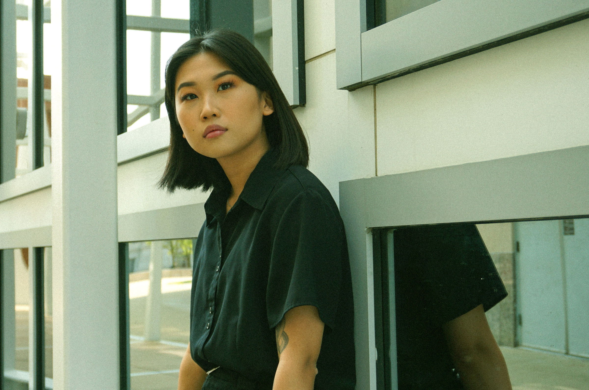 A portrait photo of Lily Li, design intern at the Wexner Center for the Arts, leaning against the side of the glass and metal grid exterior of the building