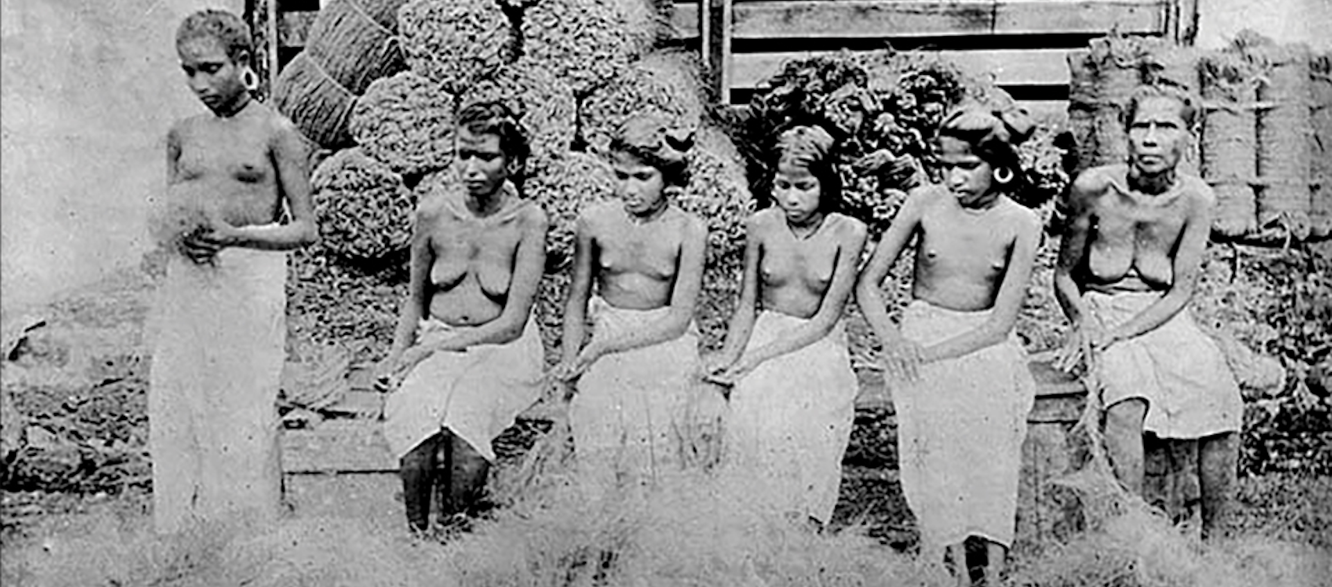 Historic archive image of six bare-breasted Indian women of various ages sitting in a row