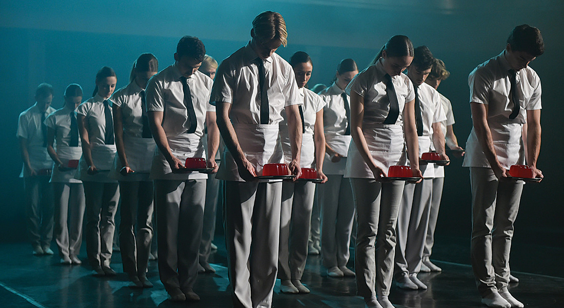 a group of young people wearing all white with black ties looking down at red jello they are holding