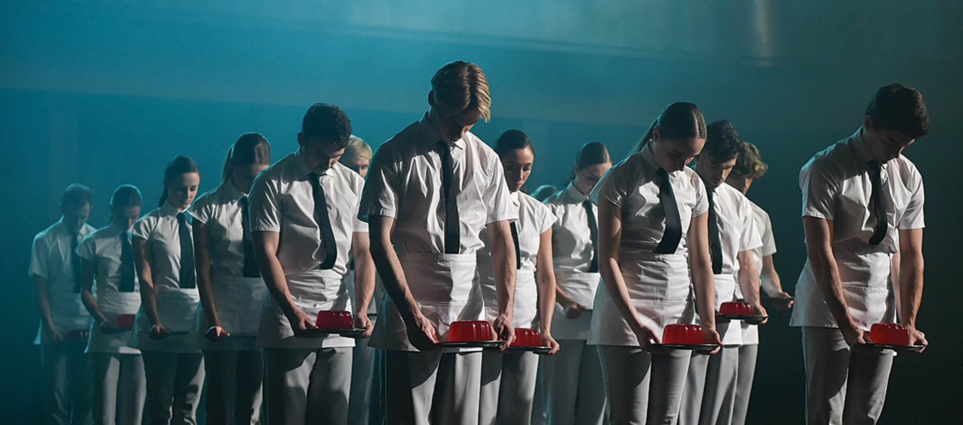 a group of young people wearing all white with black ties looking down at red jello they are holding