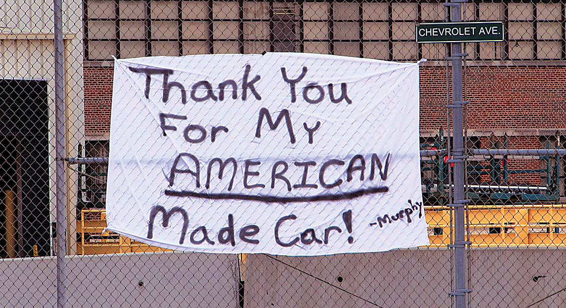 A white sheet sign hanging on a metal fence it reads Thank you for my American made car!