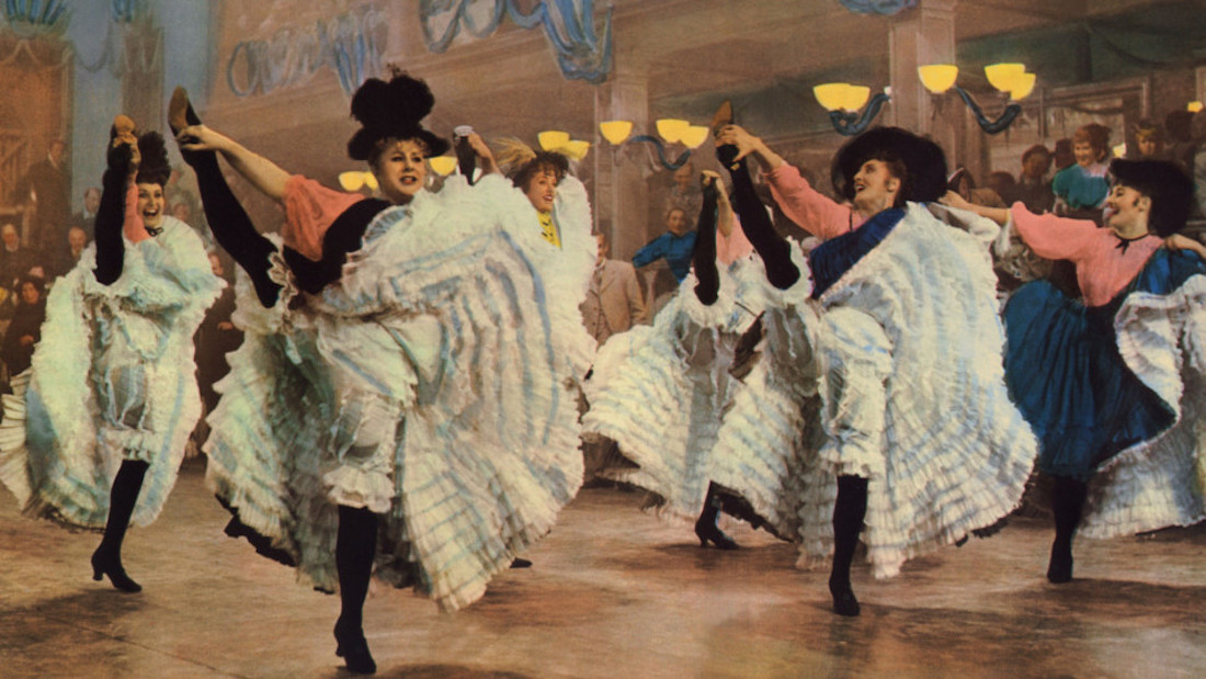 A colorful image of can can dancers kicking black-stockinged legs high, exposing frilly petticoats in a scene from John Huston's 1952 film Moulin Rouge