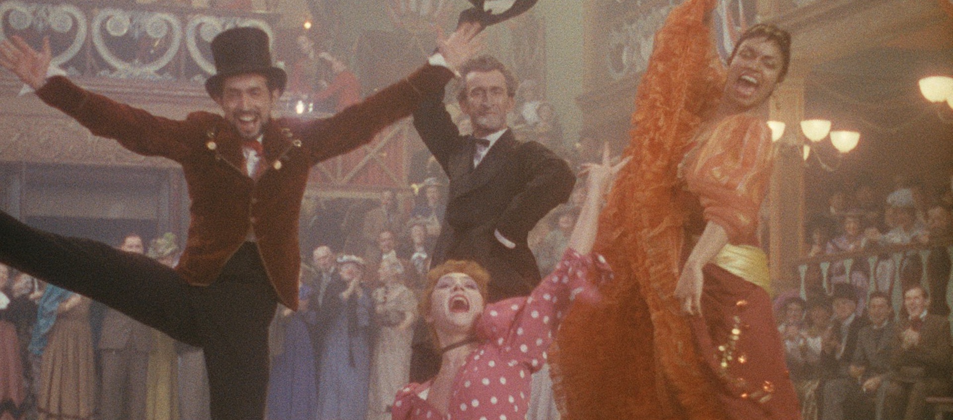 Two male and two female dancers in vintage dress face the camera with smiles and arms spread wide in a still from the 1952 John Huston film Moulin Rouge
