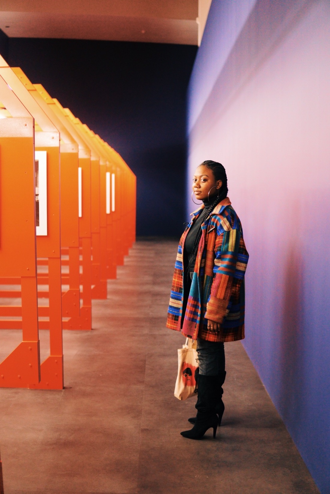 Wexner Center intern Dejiah Archie-Davis, a young woman of color wearing a bright plaid coat, standing in the installation of LaToya Ruby Frazier's The Last Cruze at the Wexner Center for the Arts. Archie-Davis is an intern at the center for Spring 2020.