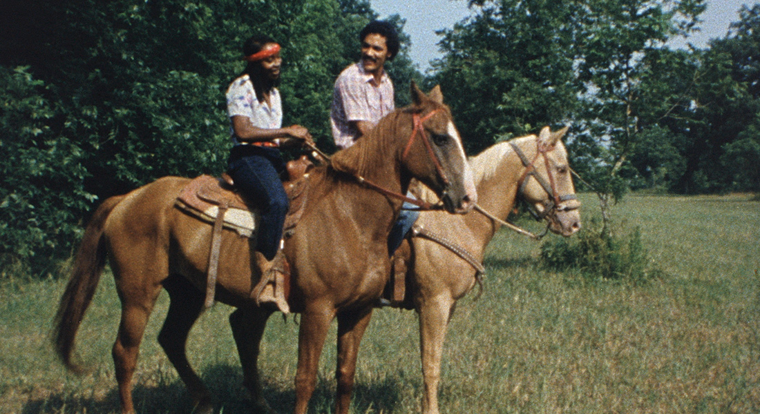 The young couple at the center of Cane River talk while riding horses together in a meadow.