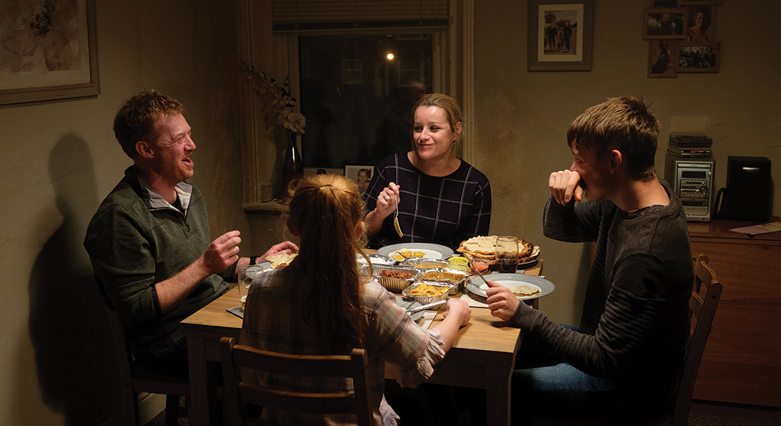 The family at the heart of film shares a laugh while seated at the table for dinner.