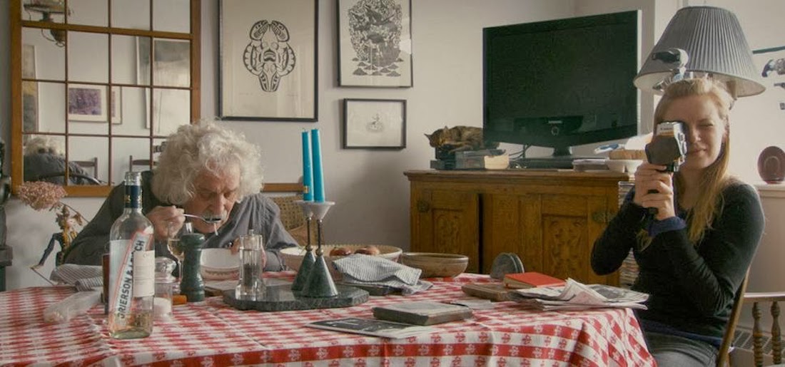 Sarah Polley points sits at a kitchen table and points a camera at the viewer in a scene from her documentary Stories We Tell