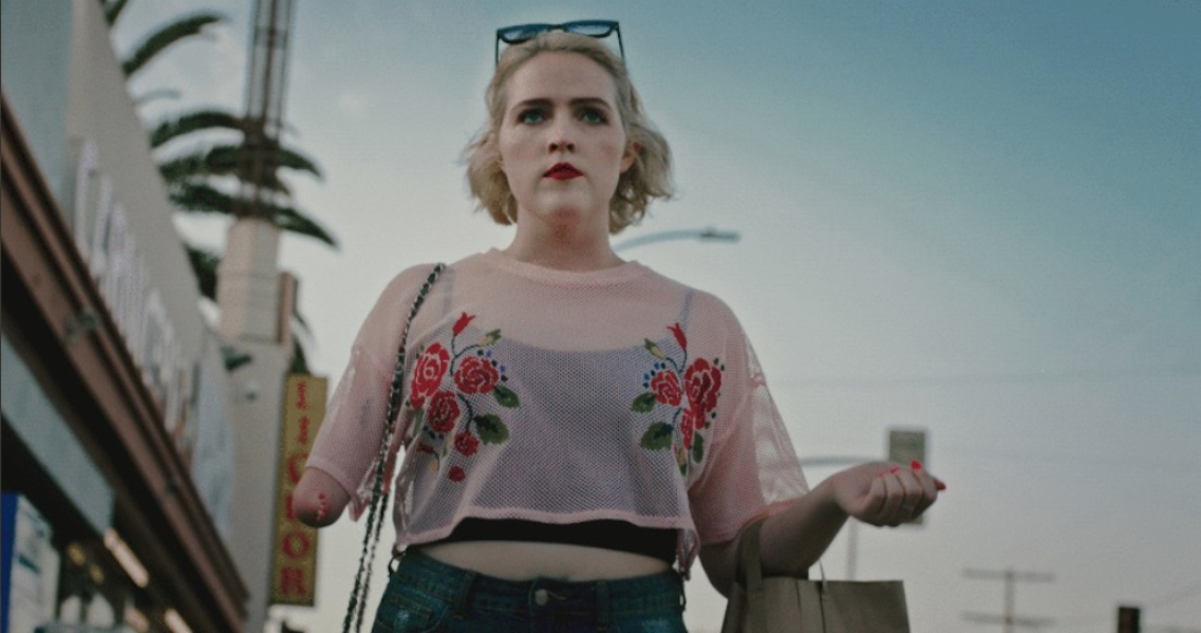 A young blonde woman born with a partially missing right arm, seen waist-up in a crop top walking outdoors in a scene from the South by Southwest short film Single by Ashley Eakin