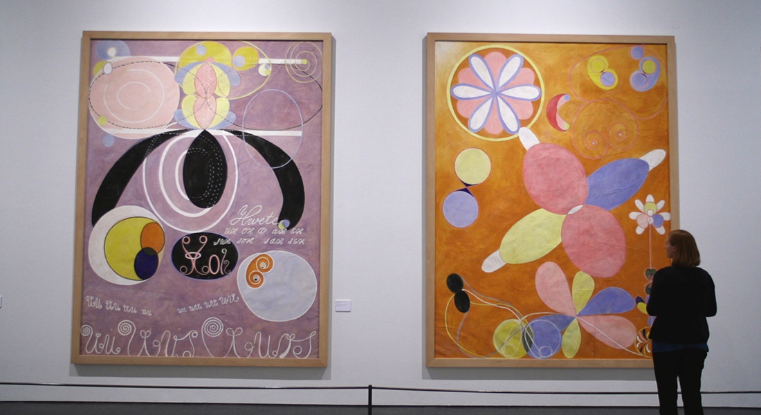 A person looking at two large abstract pieces of art by Hilma af Klint hanging in a recent exhibition