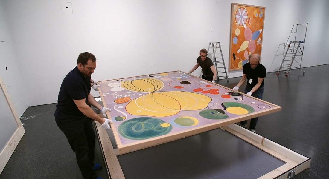 Three museum staff transferring a large work of art by Hilma af Klint with white-gloved hands