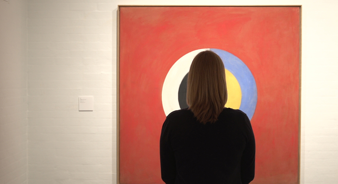 A person looking a large abstract artwork by Hilma af Klint hanging in a recent exhibition