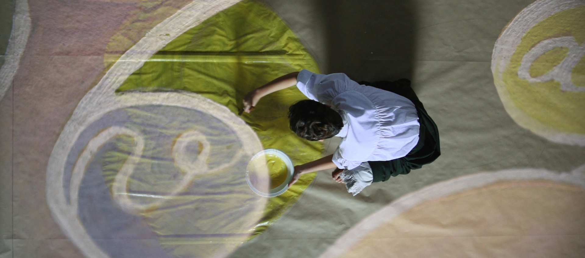 An actress reenacts artist Hilma af Klint painting a large canvas that is laid on the floor