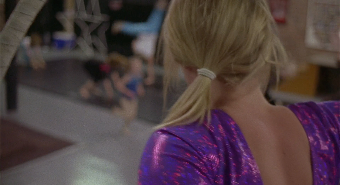 A person in a purple leotard from behind in a gym.
