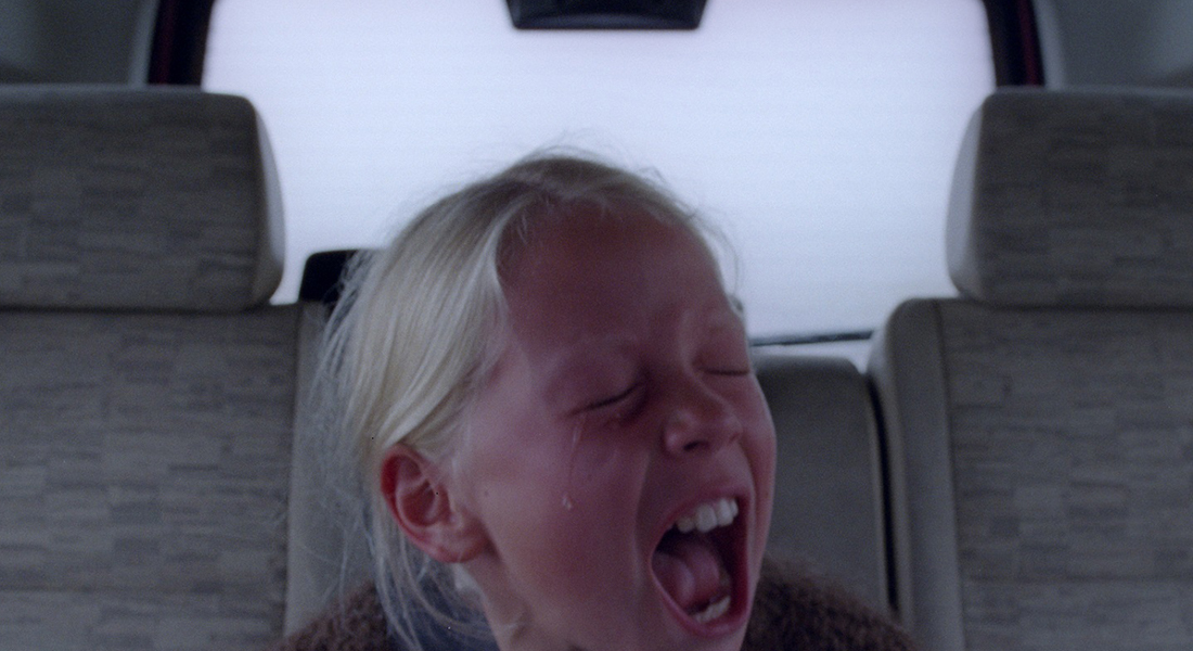 a young girl in back seat of car screaming with eyes closed and tears flowing